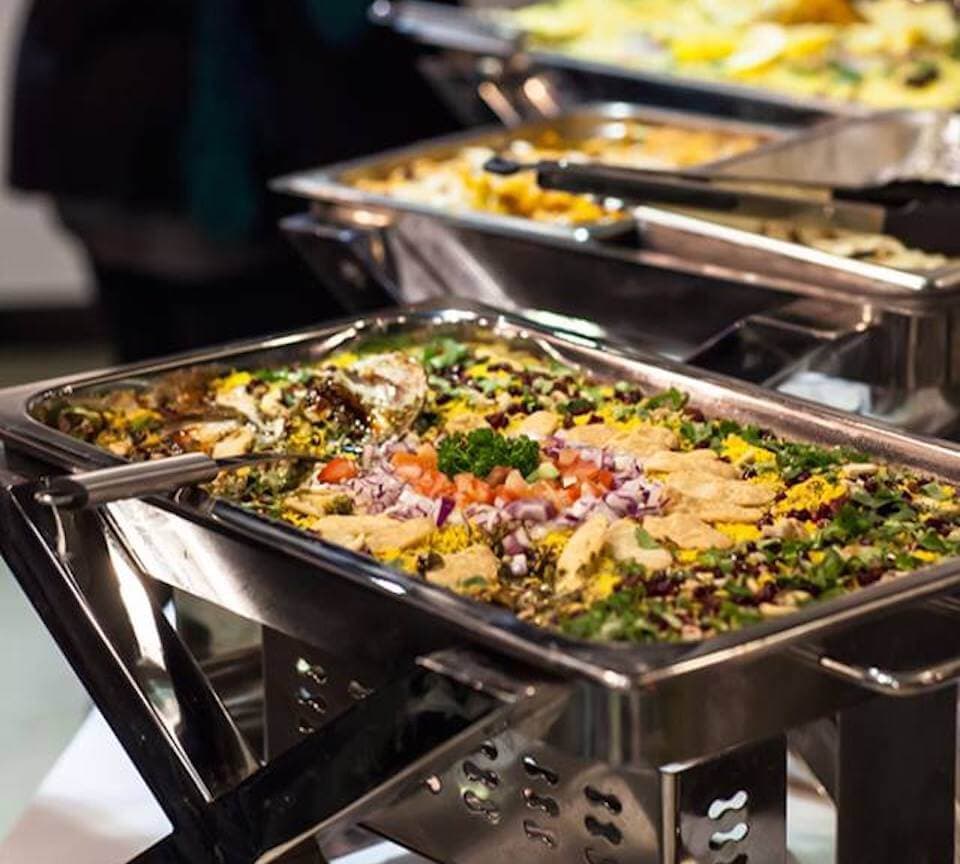Garnished rice and salad in a chafing dish on a Dosa Hut catering buffet, with further trays behind